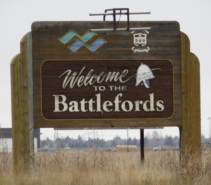 A large wooden sign in a field. In white letters, the sign reads: Welcome to the Battlefords.